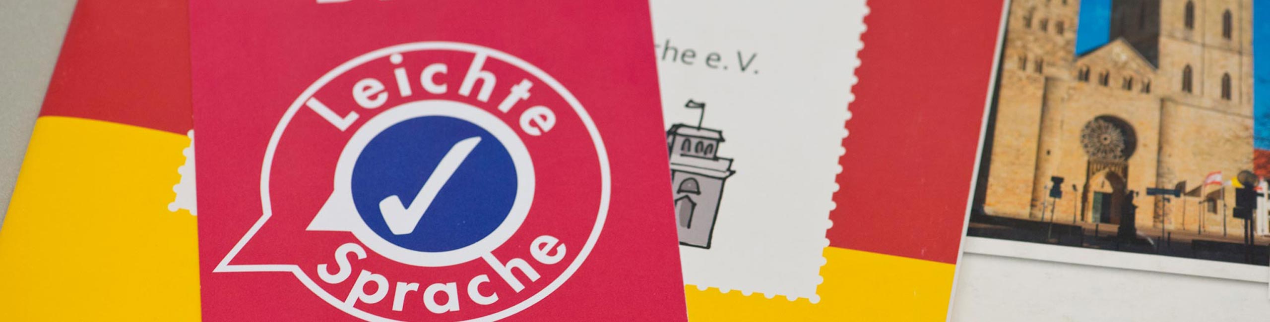Verschiedene Broschüren in Leichter Sprache. Ganz oben liegt eine rote Karte mit der Aufschrift 'Bitte Leichte Sprache'.